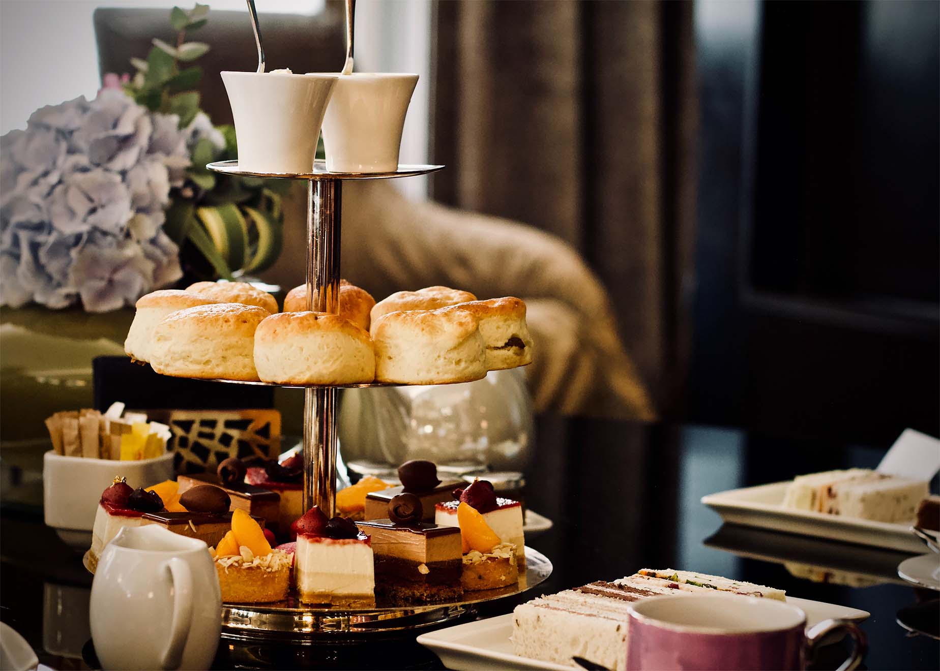 afternoon tea setup with sandwiches, scones, drinks and cakes